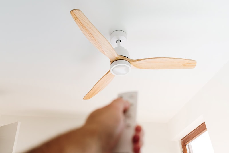 Do I Need an Electrician for Ceiling Fan Installation? Photo of a person pointing a remote to a ceiling fan.
